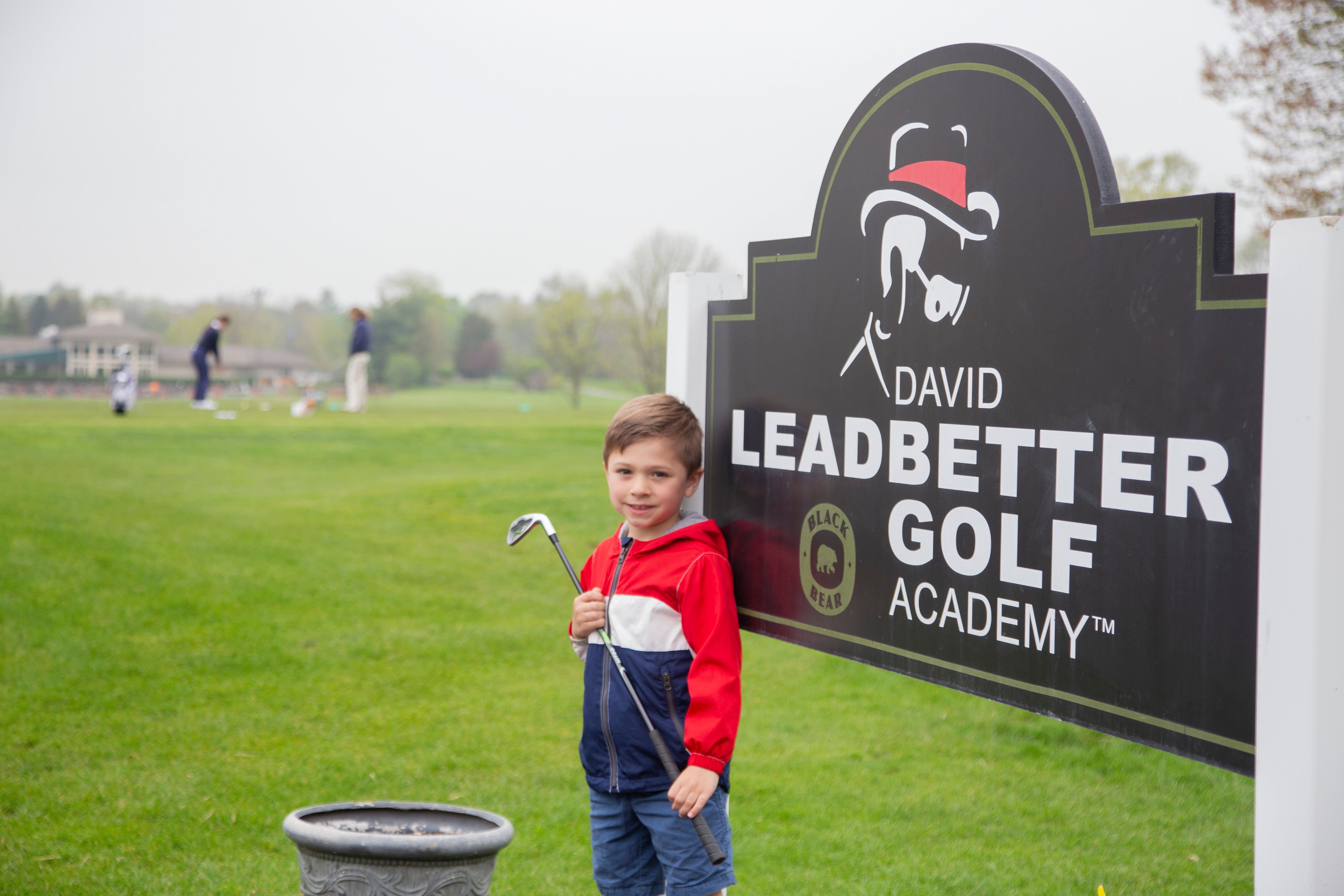 Young boy standing in front of the Leadbetter Golf Academy sign