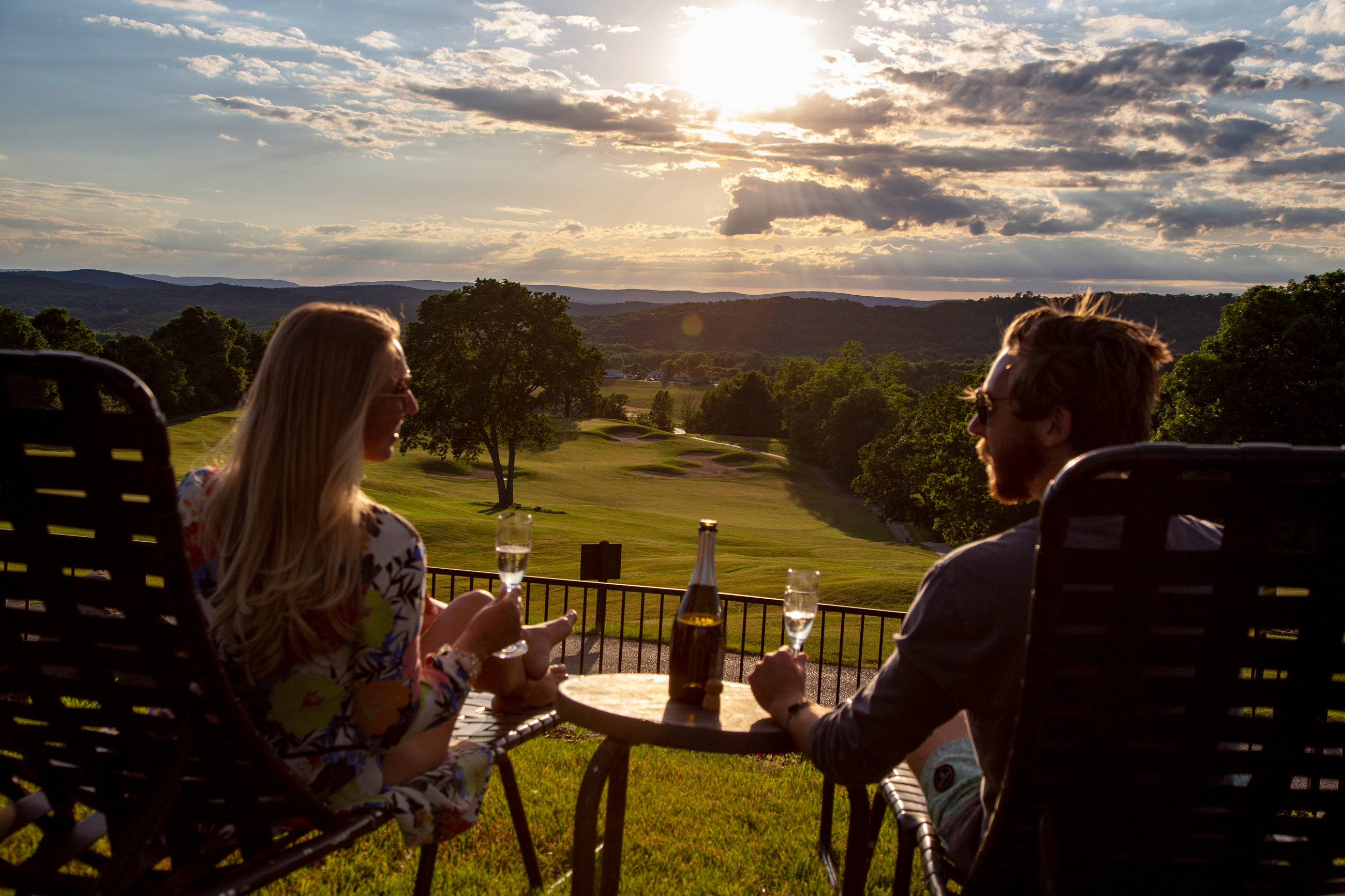 Couple drinking wine in lounge chairs at vista 180 pool looking at the sunet.