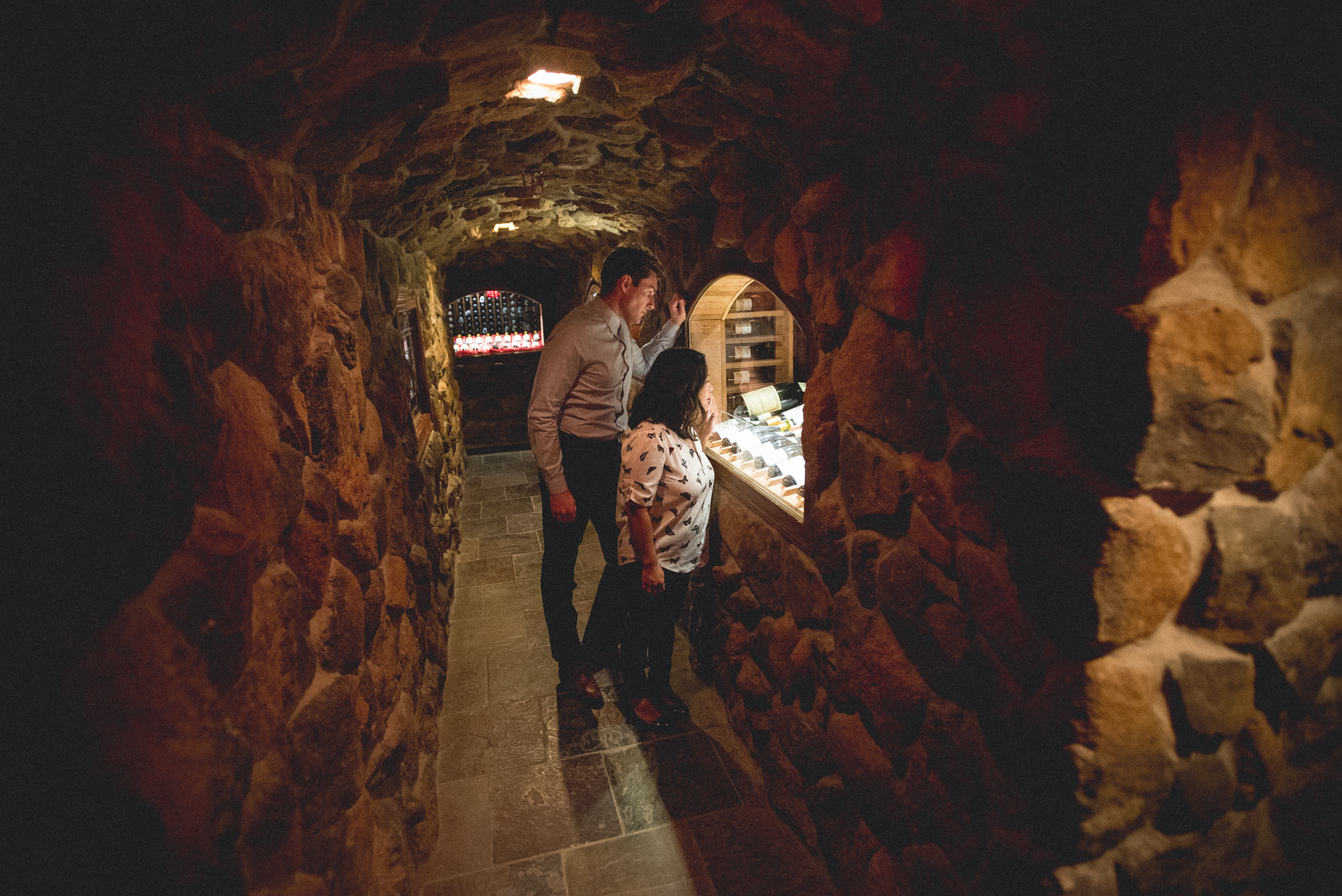 Woman and man look through glass in wine cellar to admire wine collection.