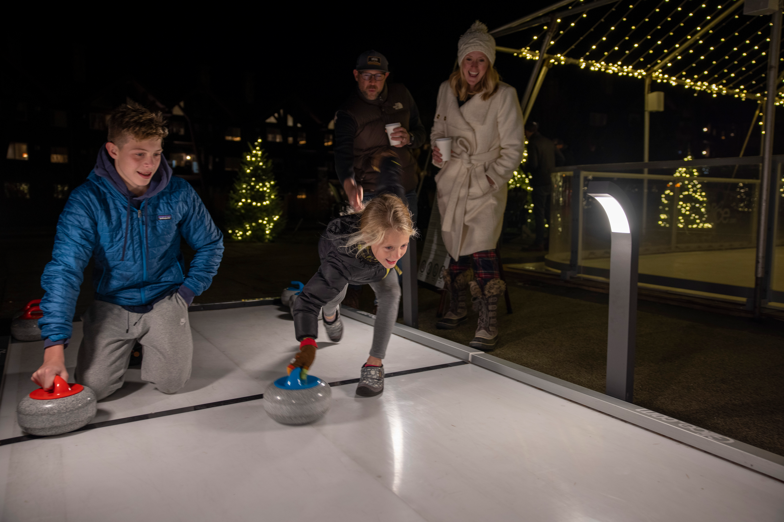 Boy and girl about to push curling stone down ice.