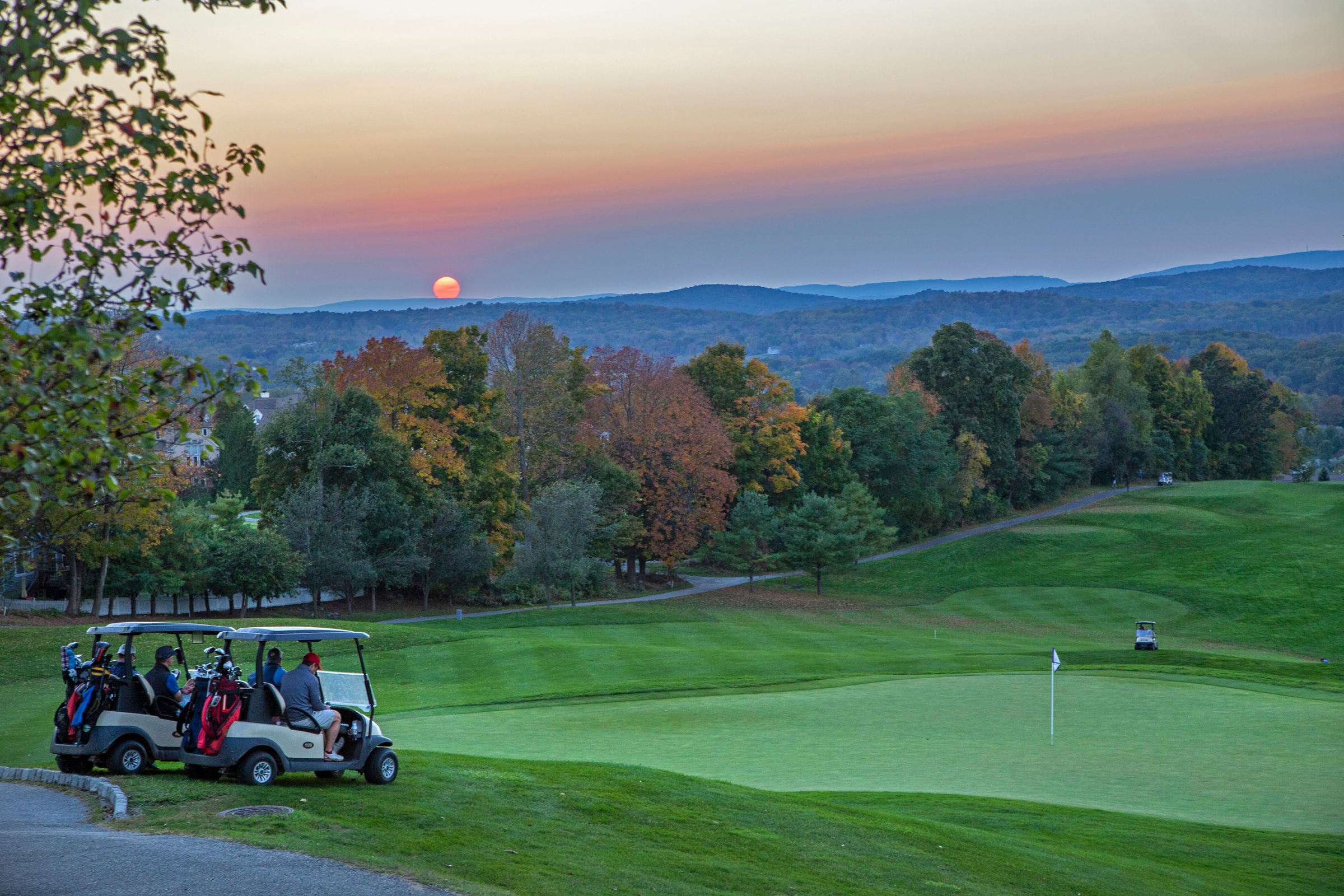 Two golf carts in front of a course during sunset