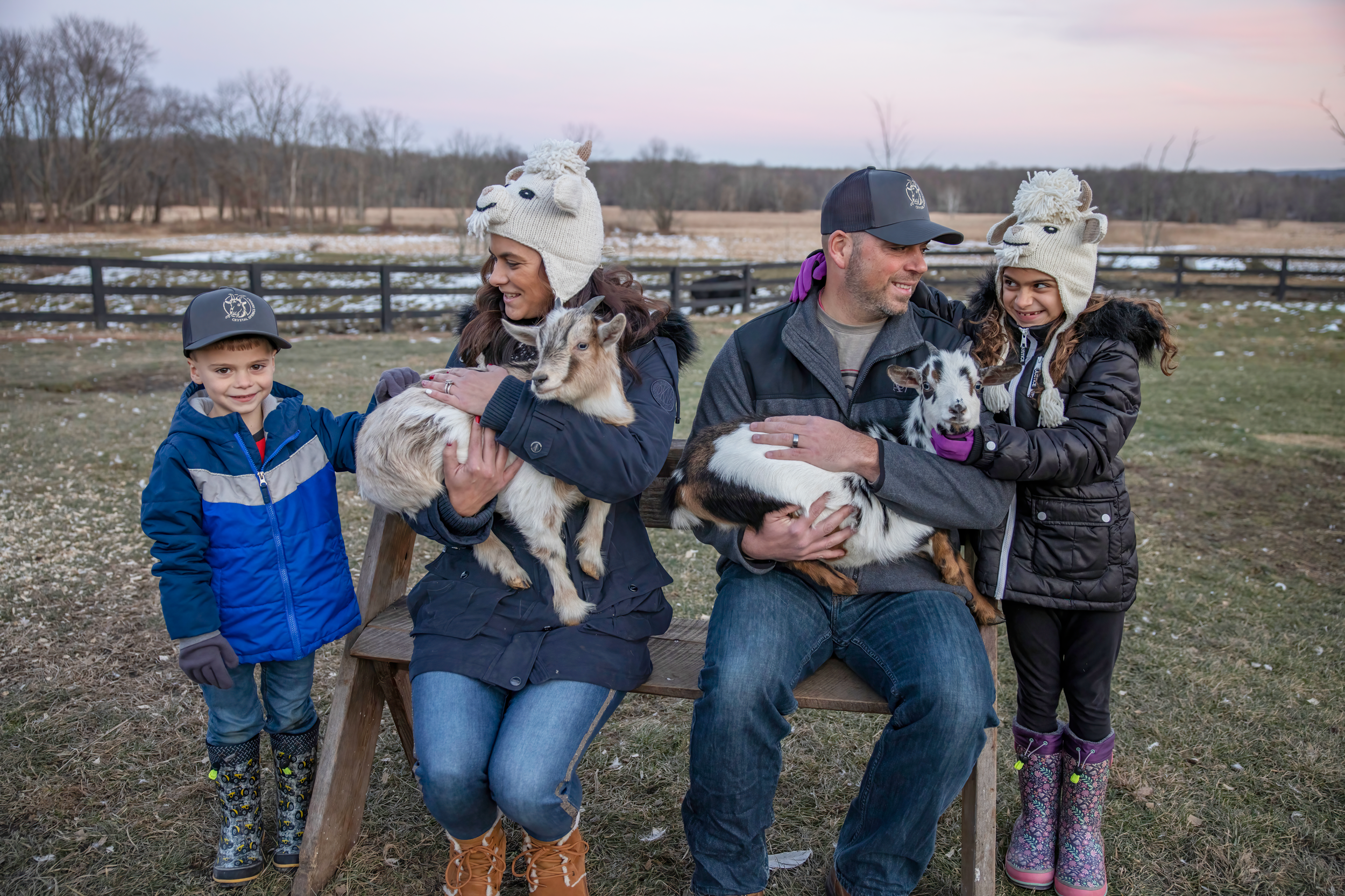 Family of four bundled up in winter clothing and holding baby goats.