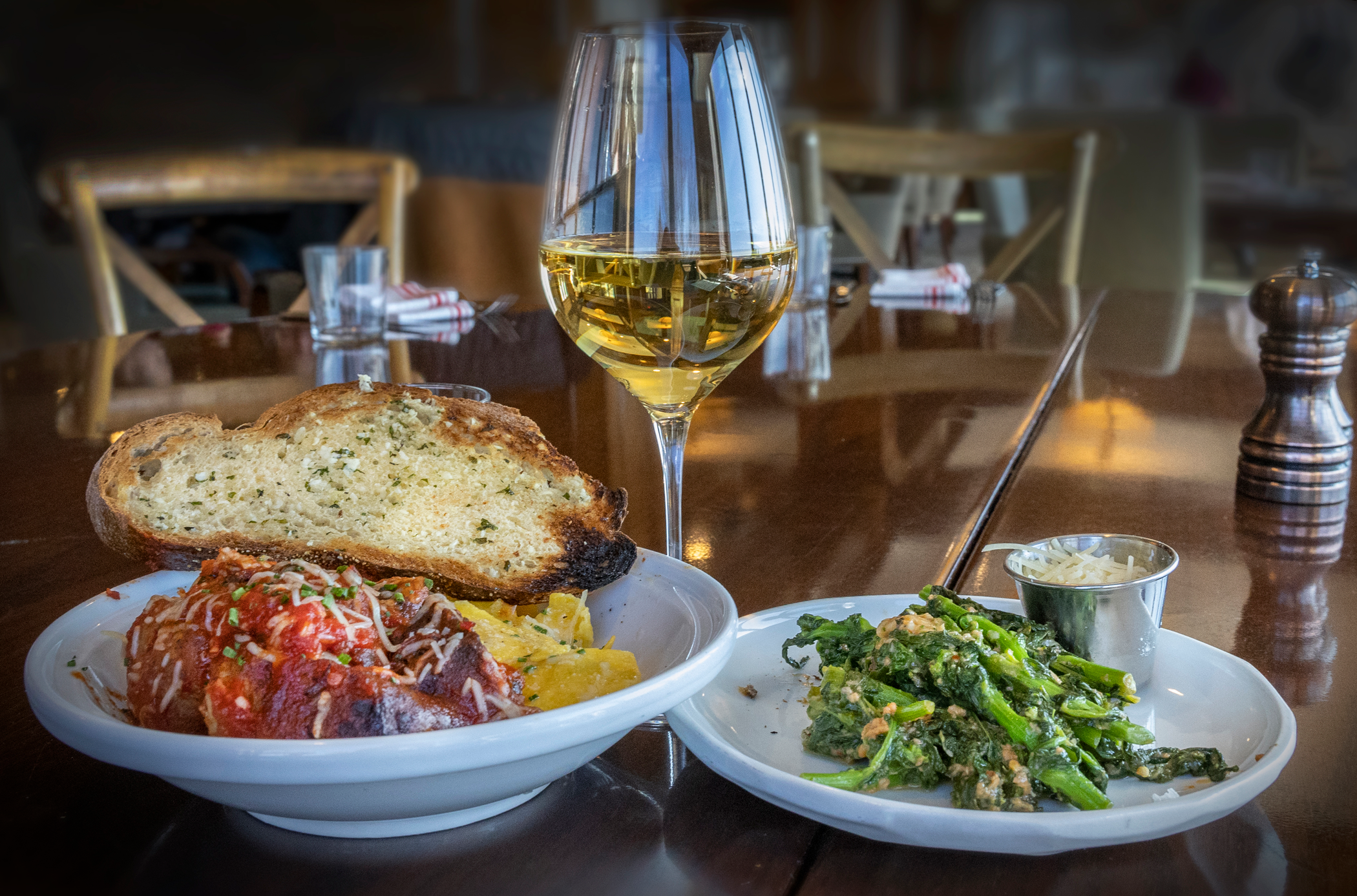 Pasta dish with side of broccoli and glass of white wine.