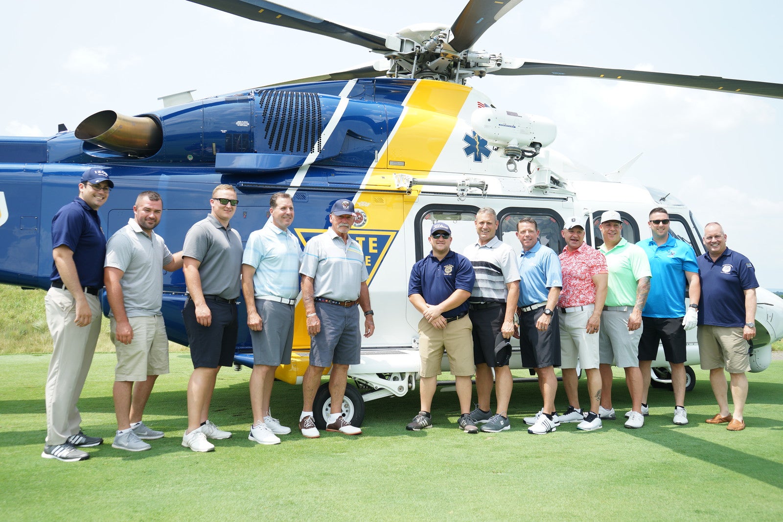 Golfers posing in front of NJ State Police helicopter.