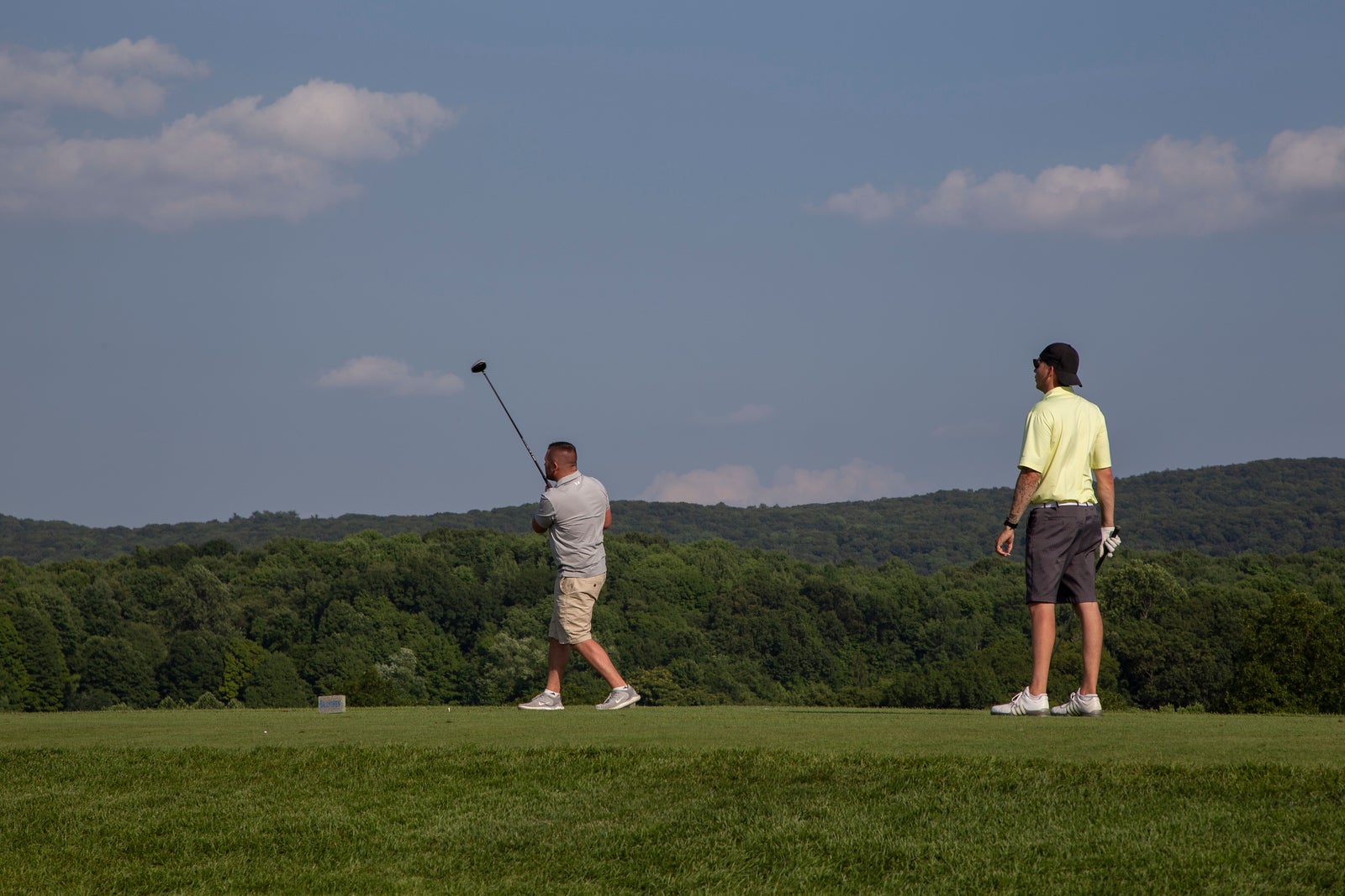 Golfer teeing off with mountain views in the distance.