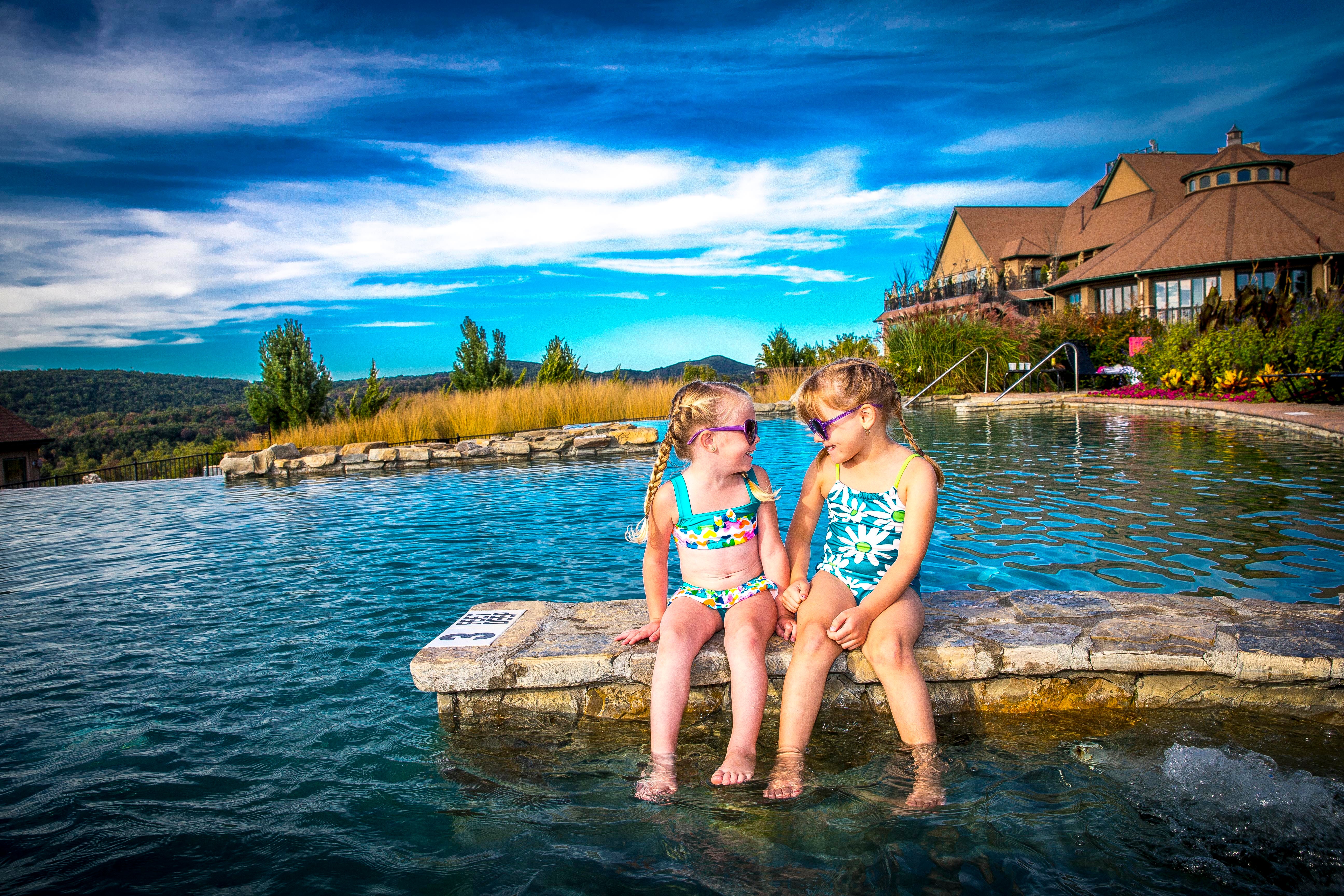 Two young girls wearing sunglasses and sitting at the Vista 180 pool.