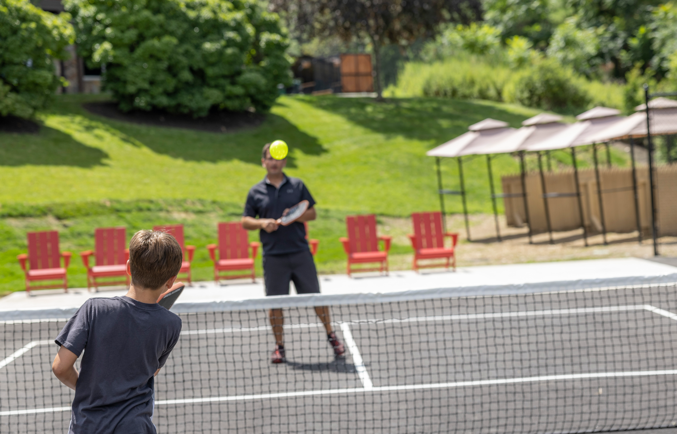 Child playing pickleball with father.