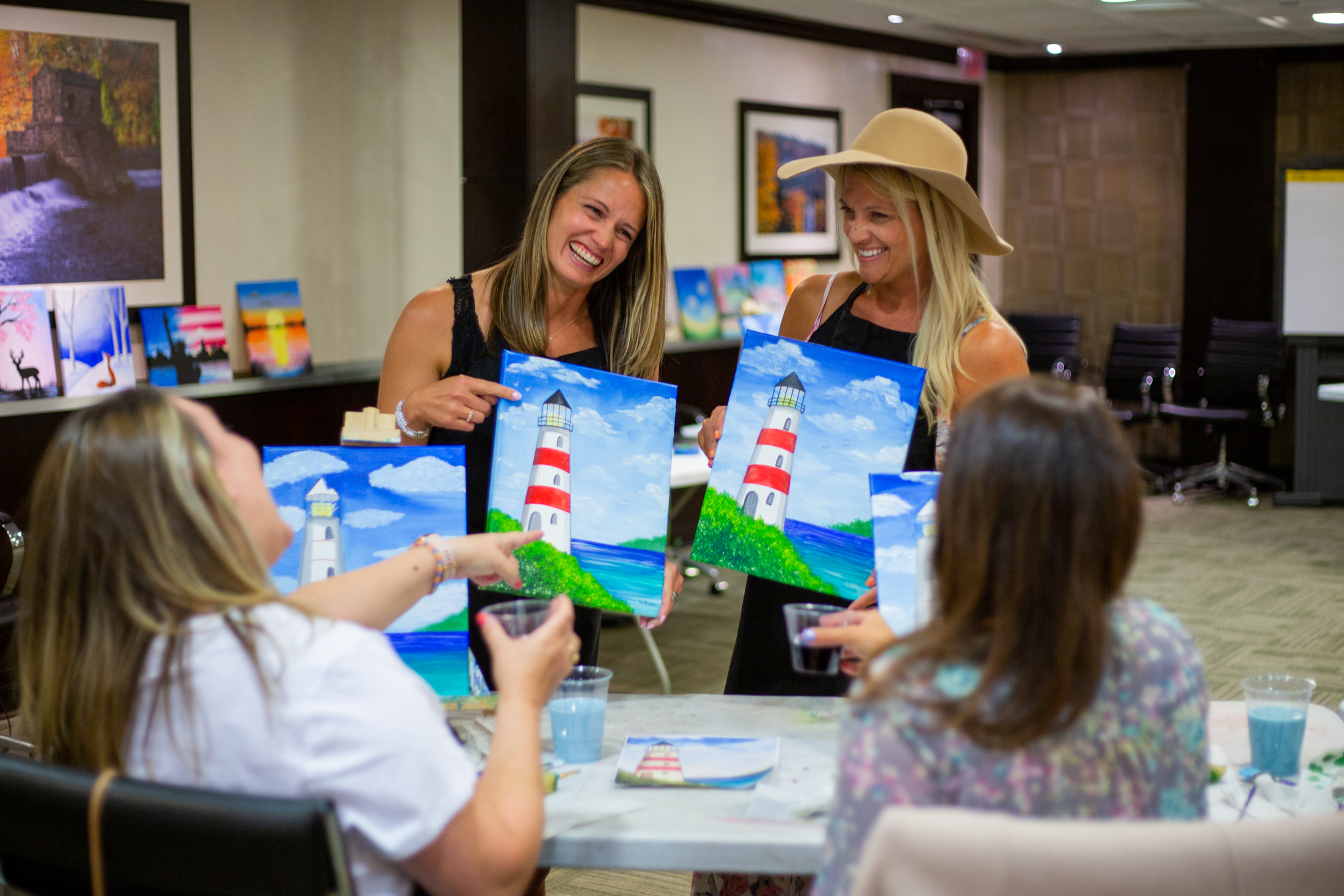 Four girlfriends showing their lighthouse painting from the Paint &amp; Sip activity.
