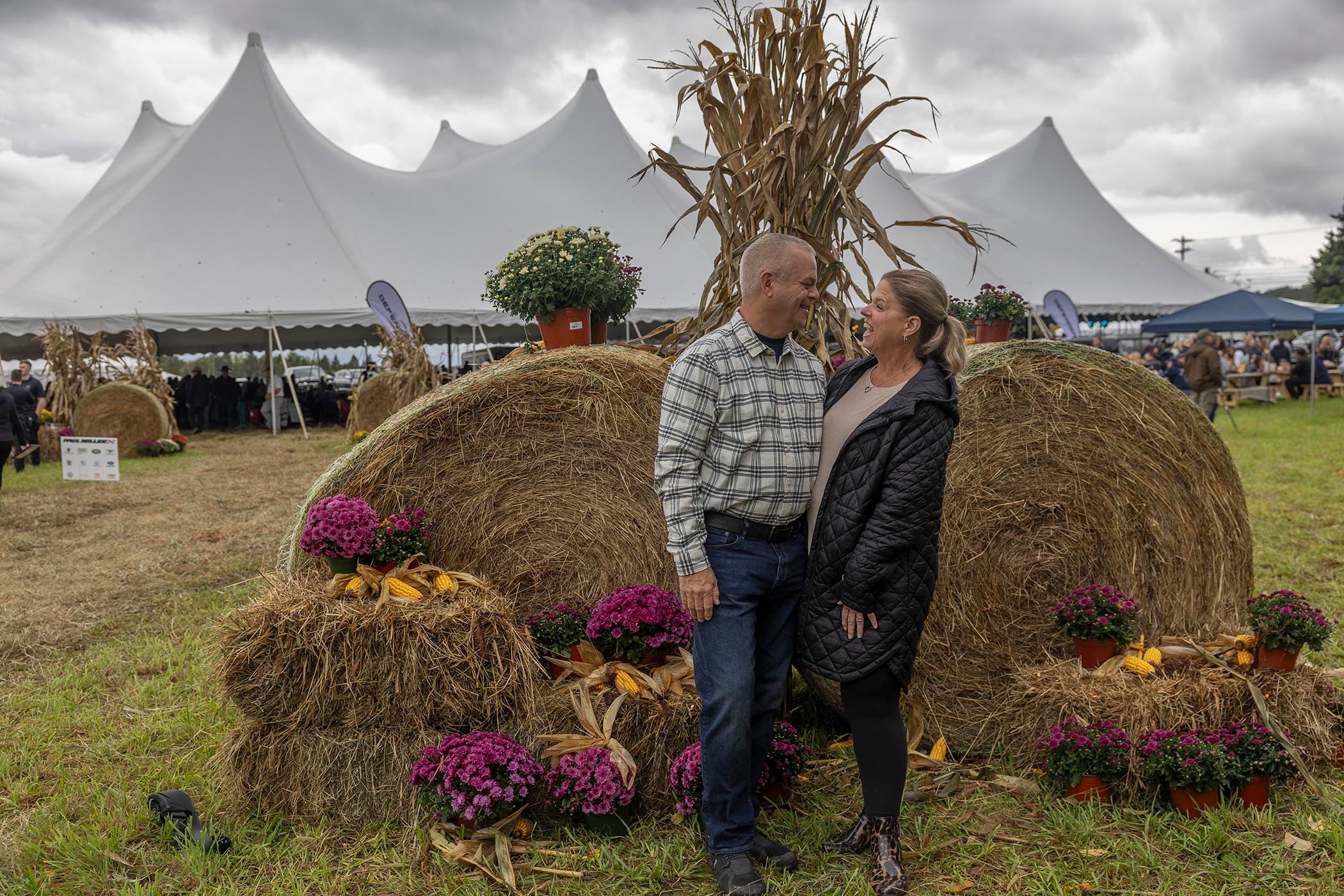 Couple standing in front of two large hay bales.