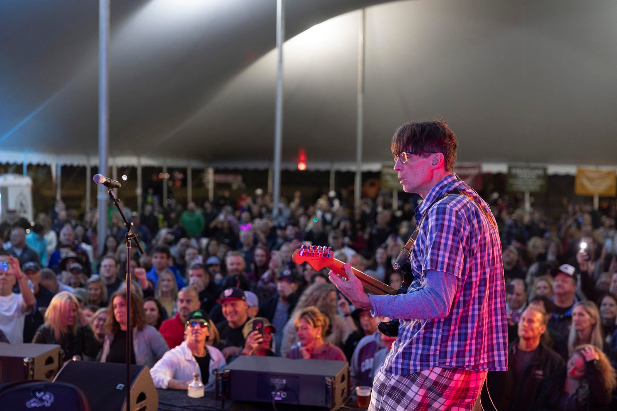 Man playing guiatr on music fest stage with large crowd in front of him
