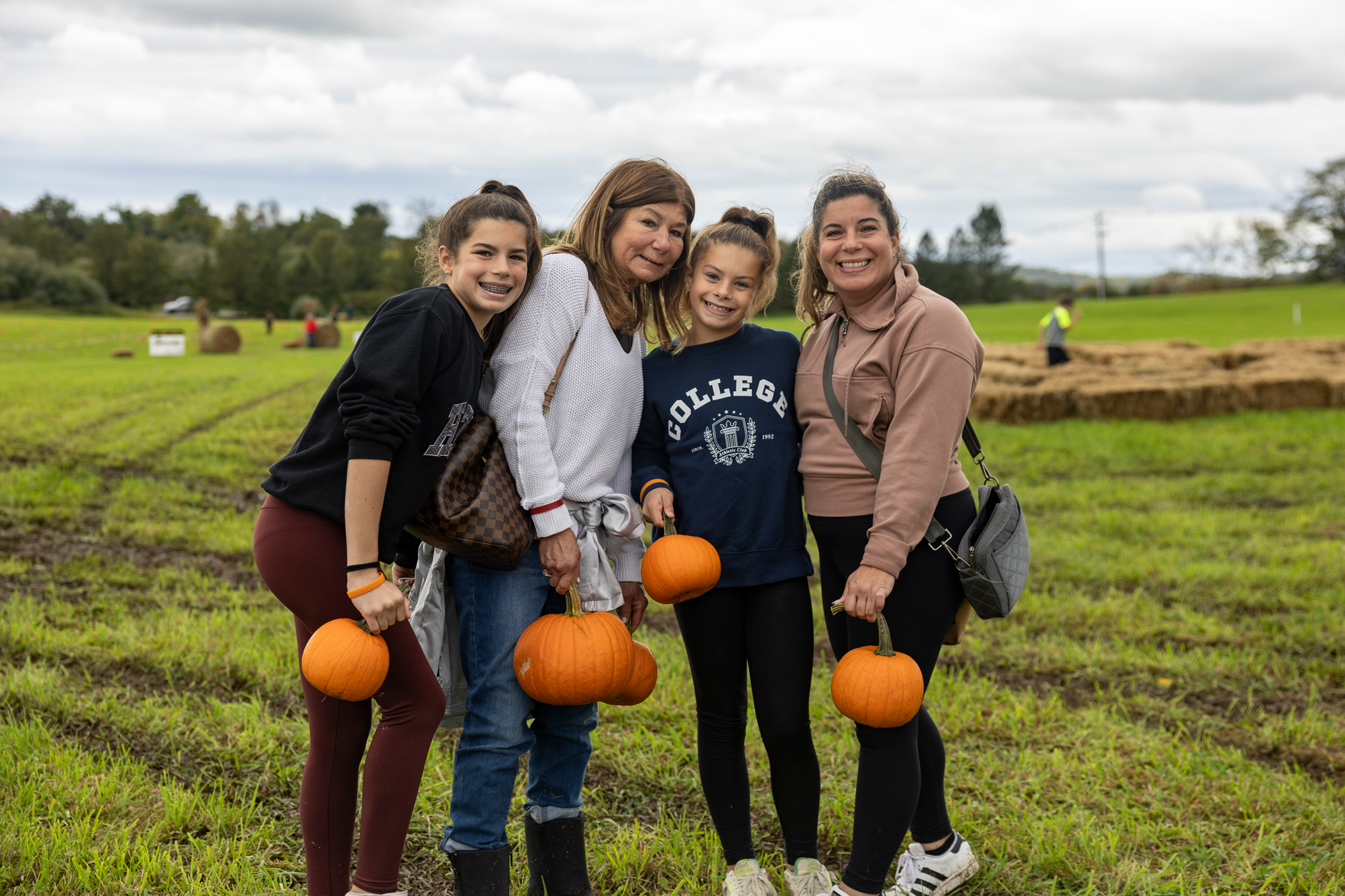 Two women and two children standing in an open field holding pumpkins.