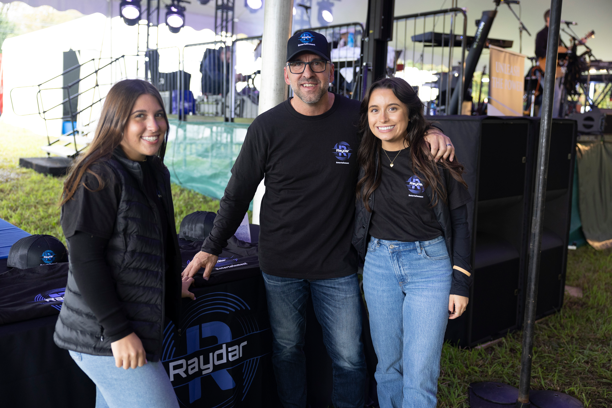 Two women and a man standing in front of Raydar Entertainment sign.