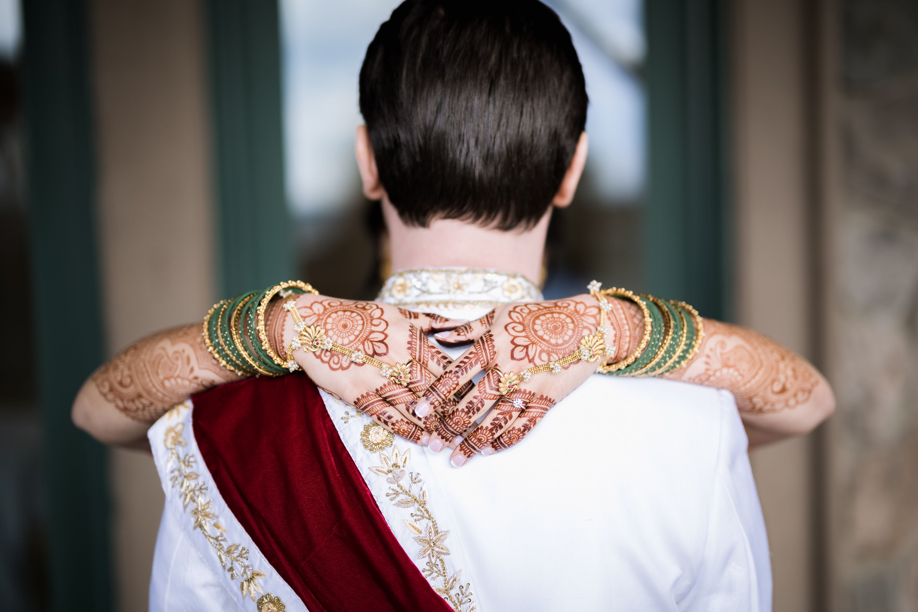 Woman, with henna on her hands, wraps her hands arounds grooms neck.