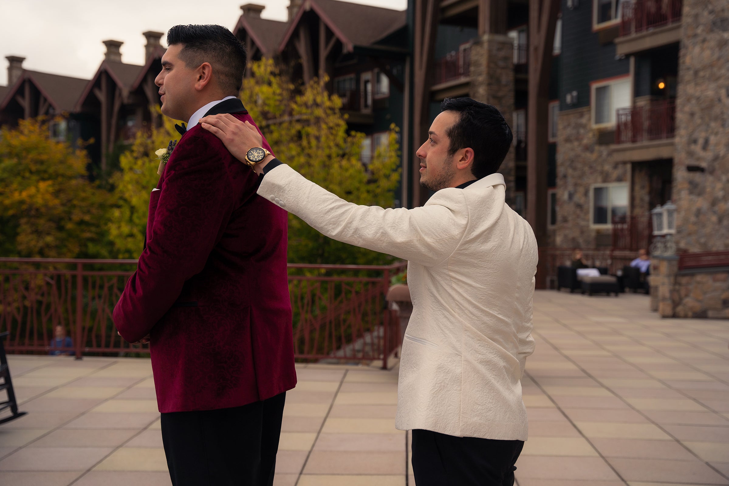 Groom wearing a white jacket, places hand on husbands shoulder during first look.