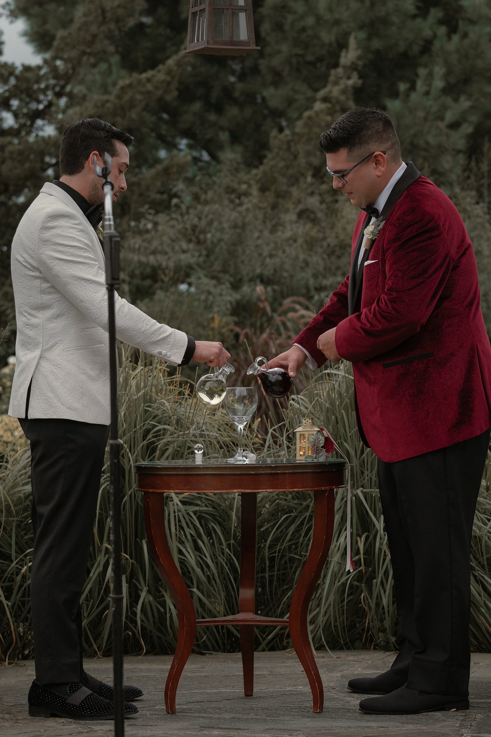 Two grooms pouring wine in glass during ceremony.