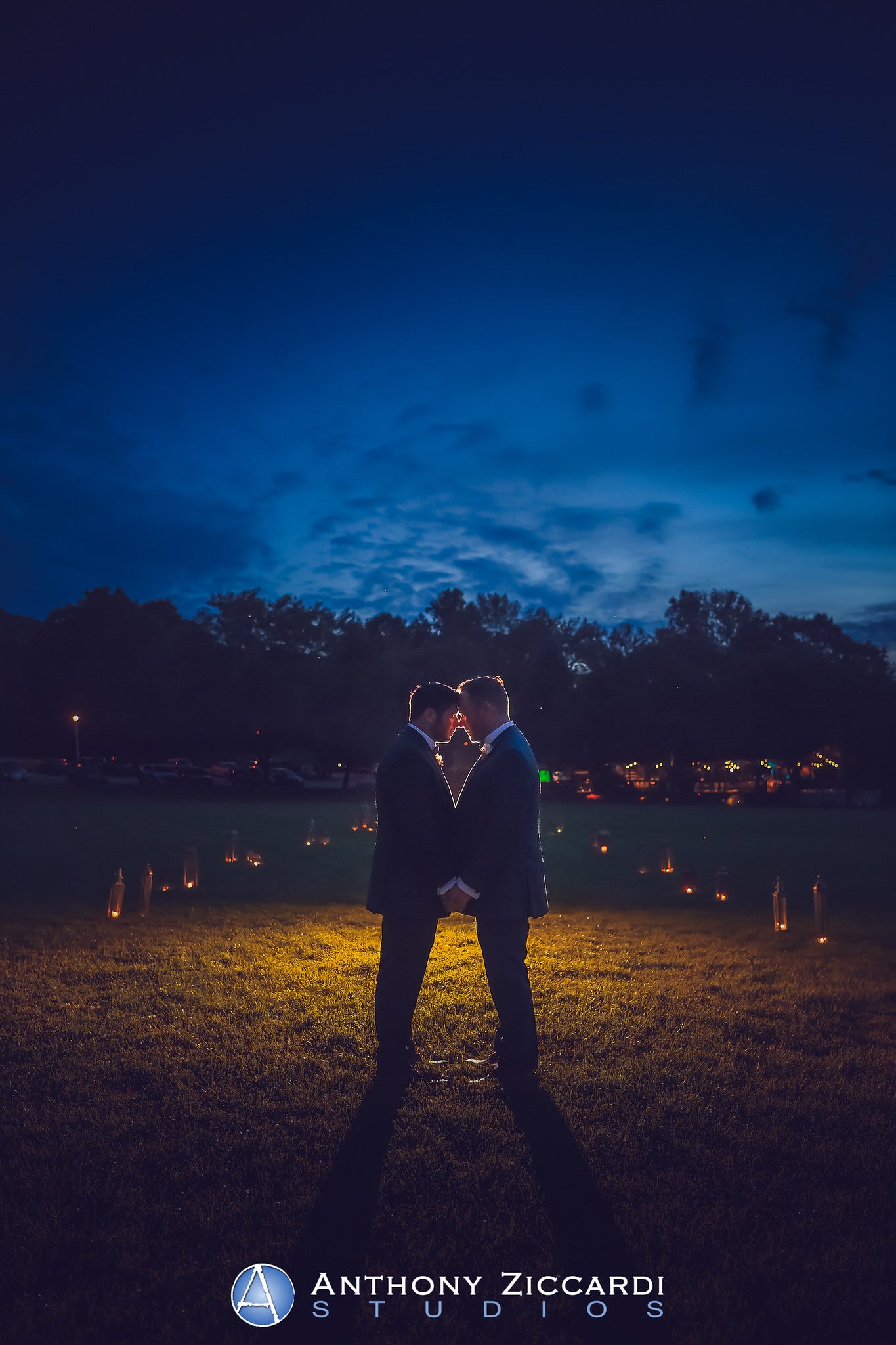 Grooms with foreheads placed together standing in a candle lit walkway.