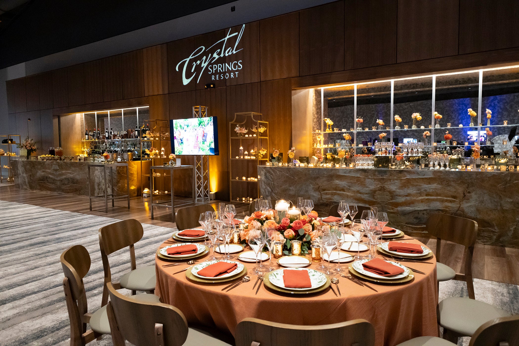 Canyon Ballroom table set up with orange flowers and napkins with bar featured in back.