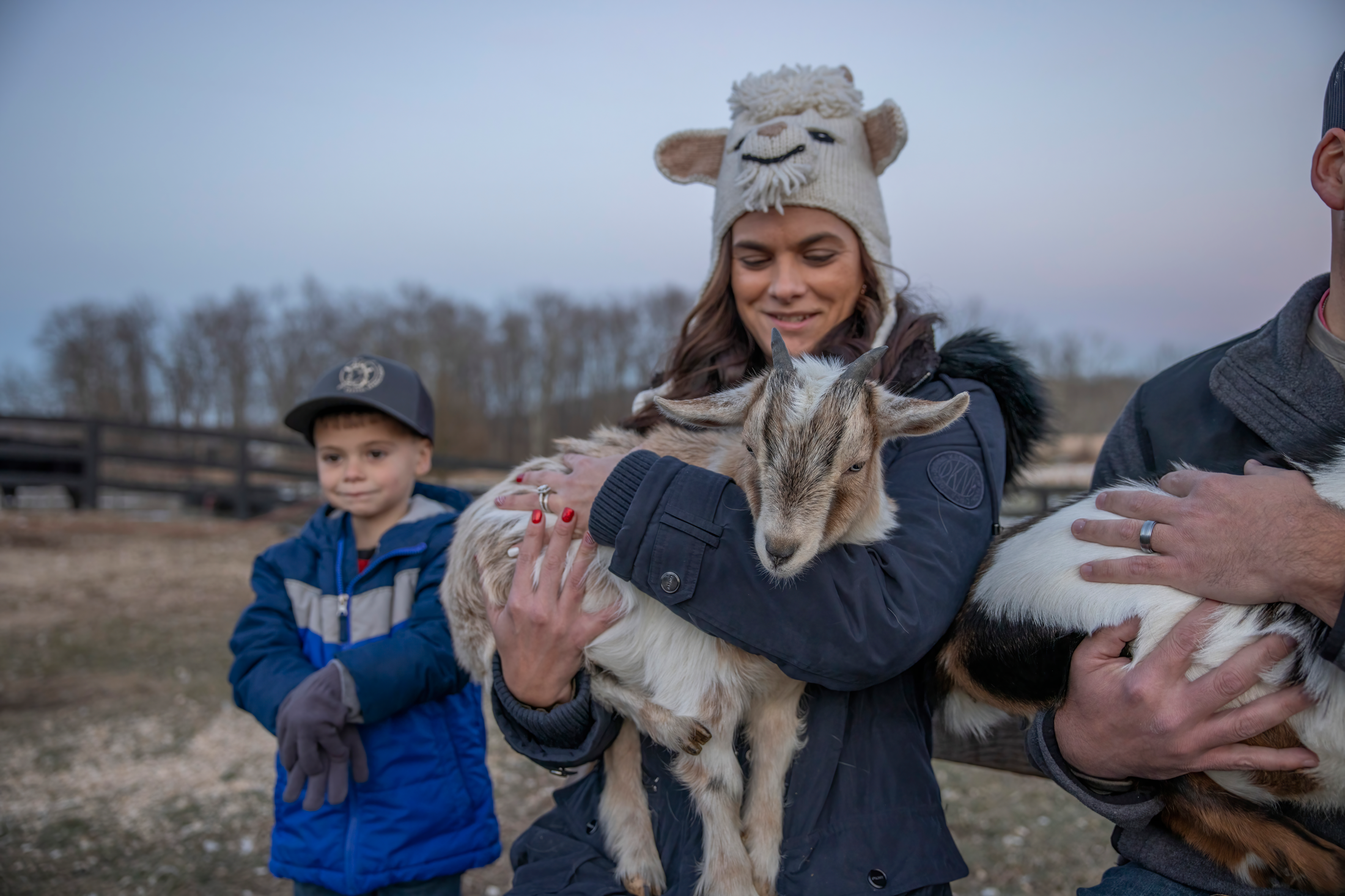 Woman wearing a goat hat holding a baby goat.