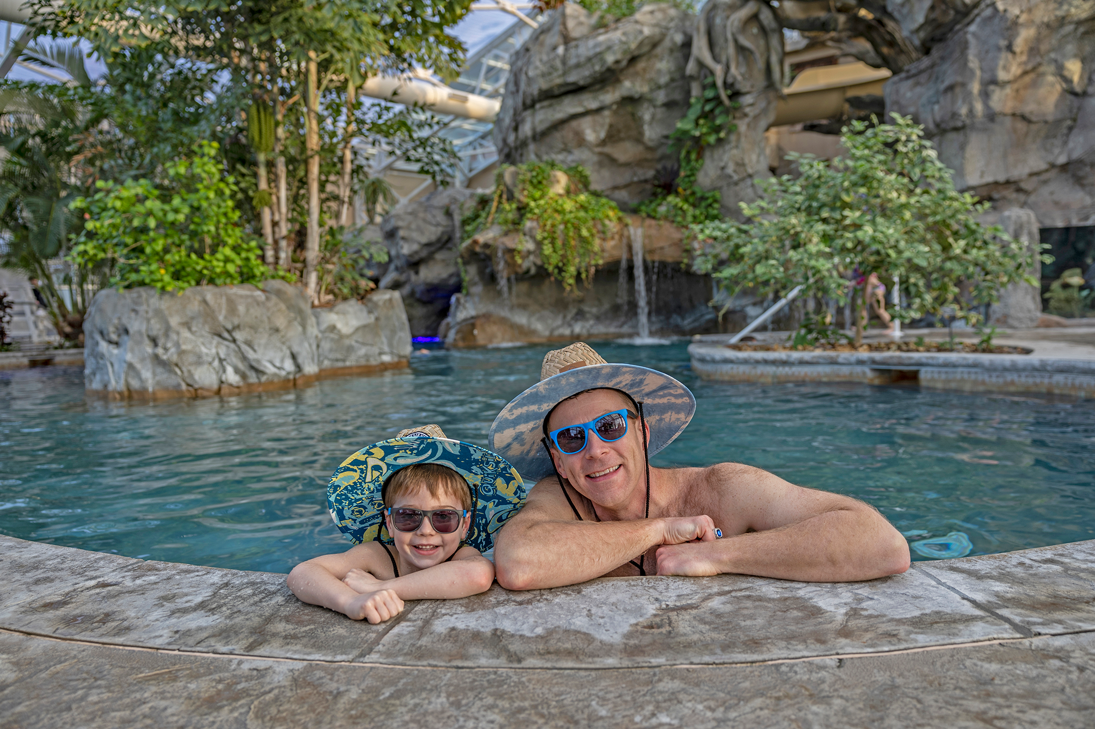 Father and son wearing matching hats and sunglasses in Biosphere pool.
