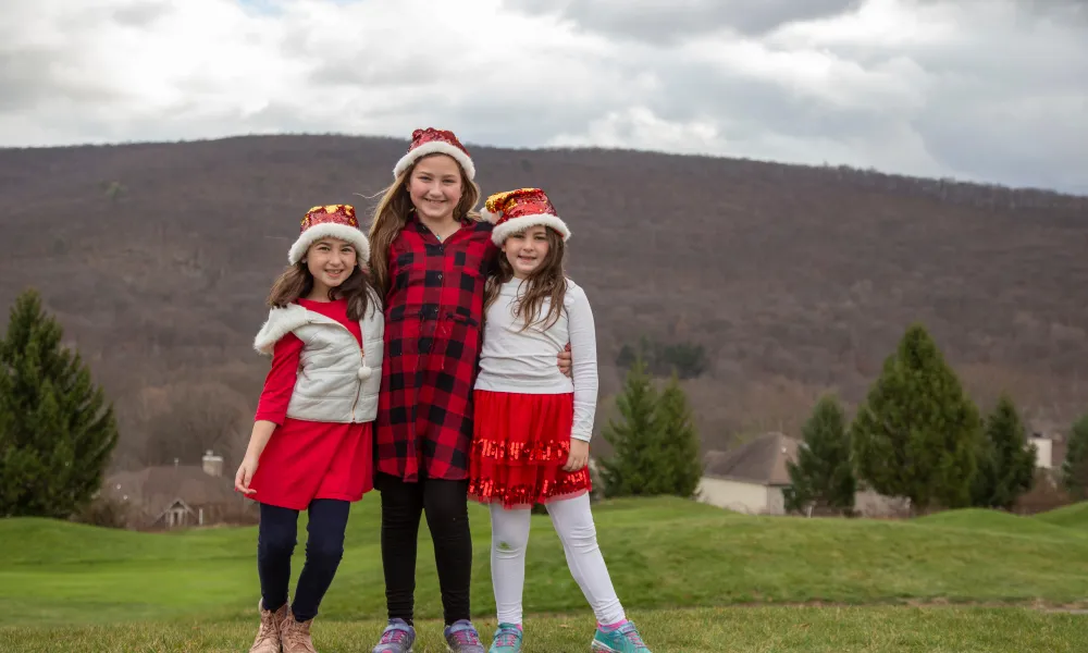 Three girls in holiday outfits posing for a photo with mountains in the background.