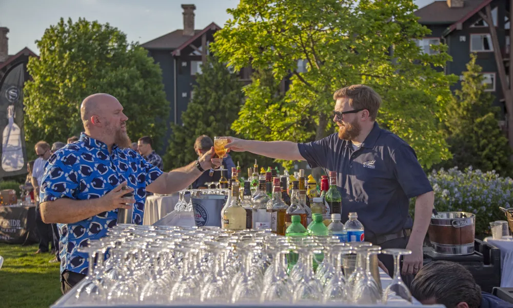 Bartending handing guest a cocktail at outdoor bar. 
