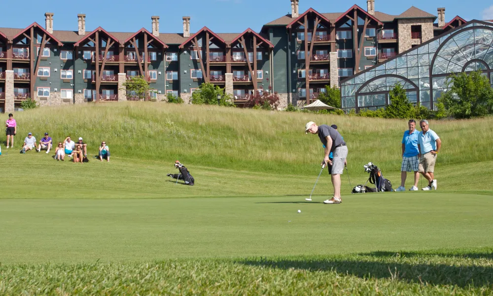 Man hitting a golf ball in front of Grand Cascades Lodge