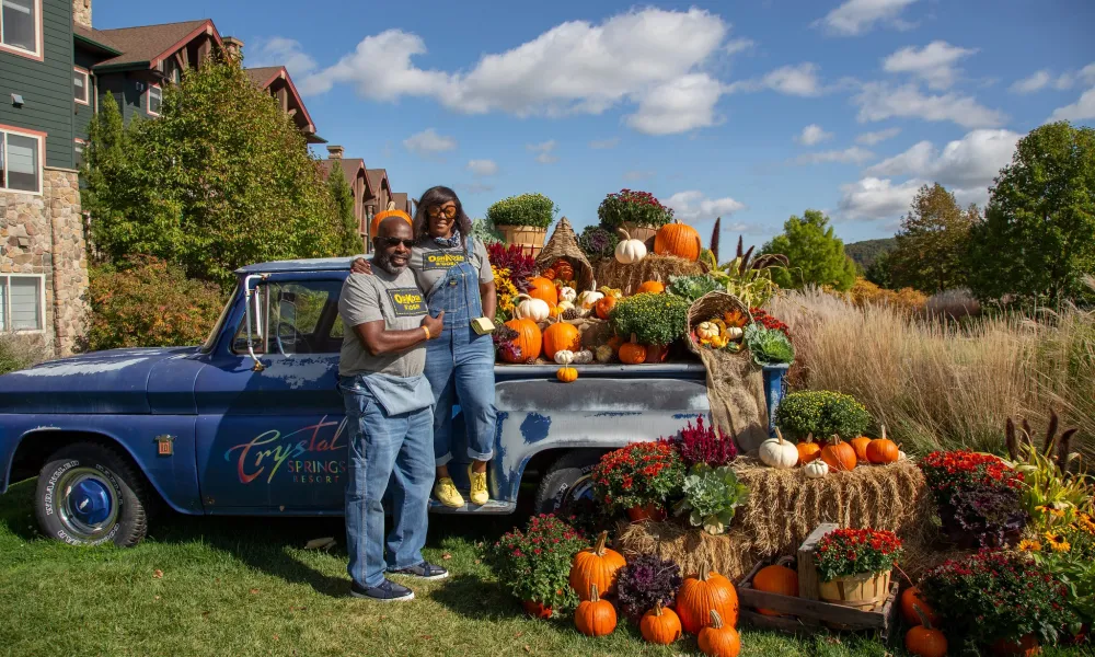 Couple posing in front of blue truck with fall decorations.
