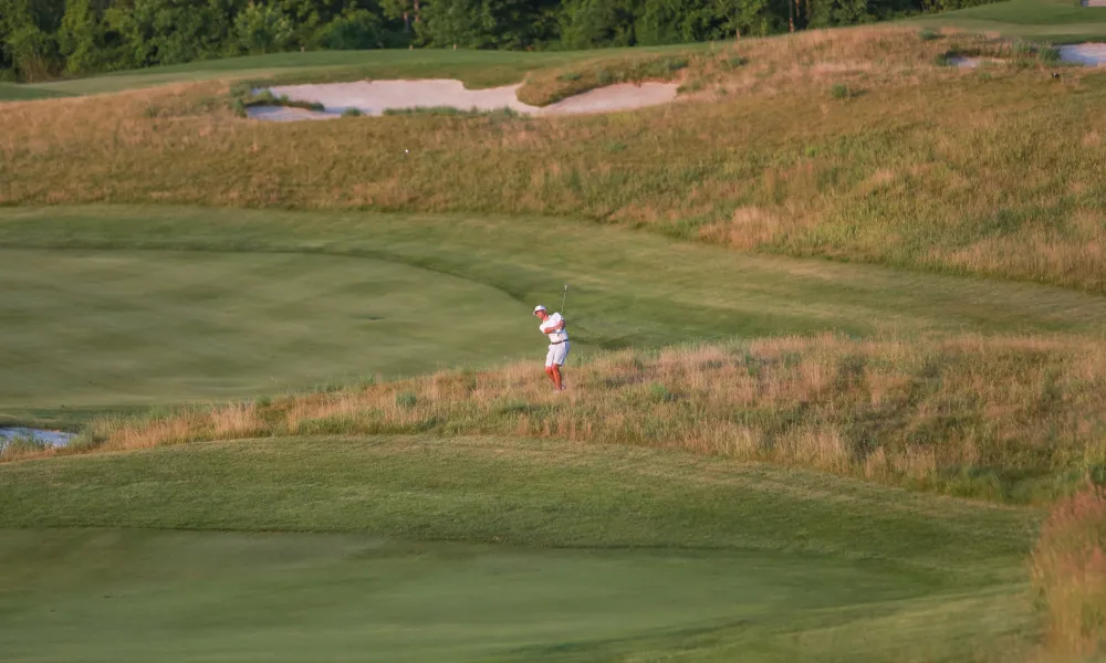 Man swinging golf club on course. 