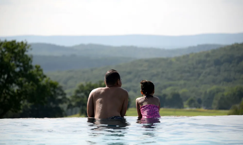 Father and daughter look out over valley while in Vista infinity pool.