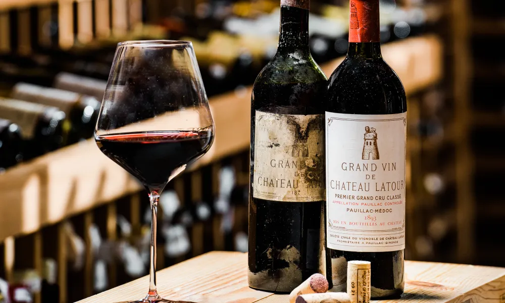 Two bottles of wine and one wine glass filled with red wine. 