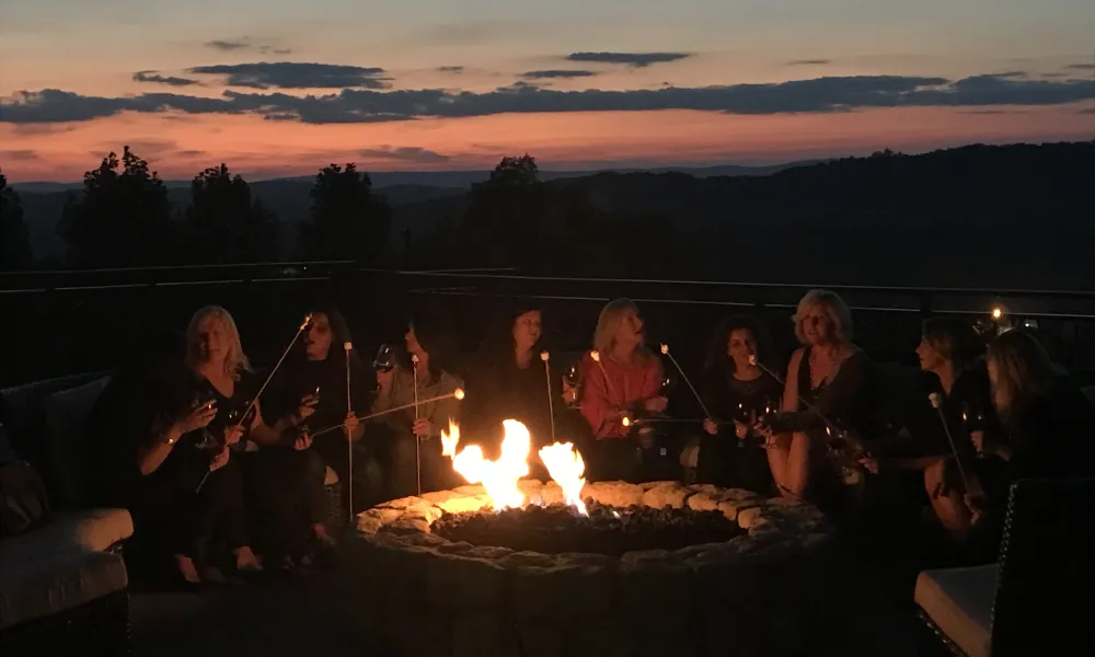 Group Roasting Marshmallows around Fire Pit on fire and water terrace at Grand Cascades Lodge.