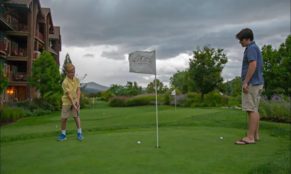 A young child in a yellow shirt playing with his father on the putting green at Grand Cascades Lodge