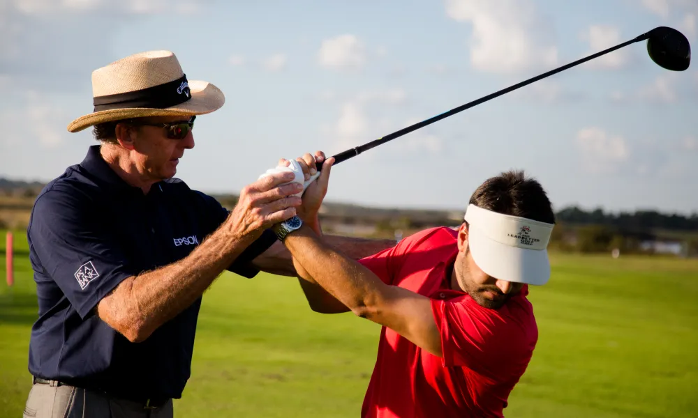 Golf instructor giving lessons to man in red shirt