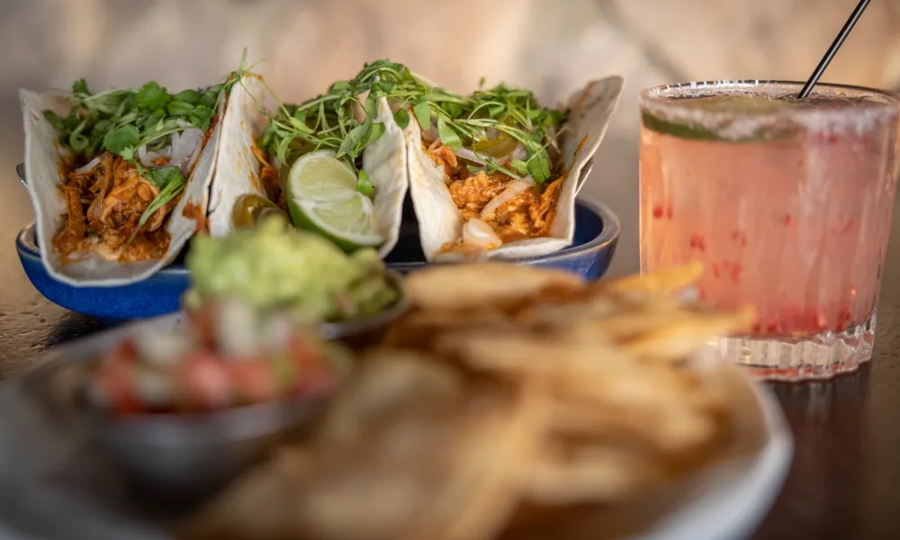 Three tacos with pink margarita on side.