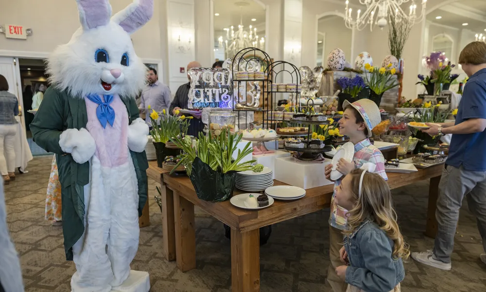 Two children standing with easter bunny in front of food display.