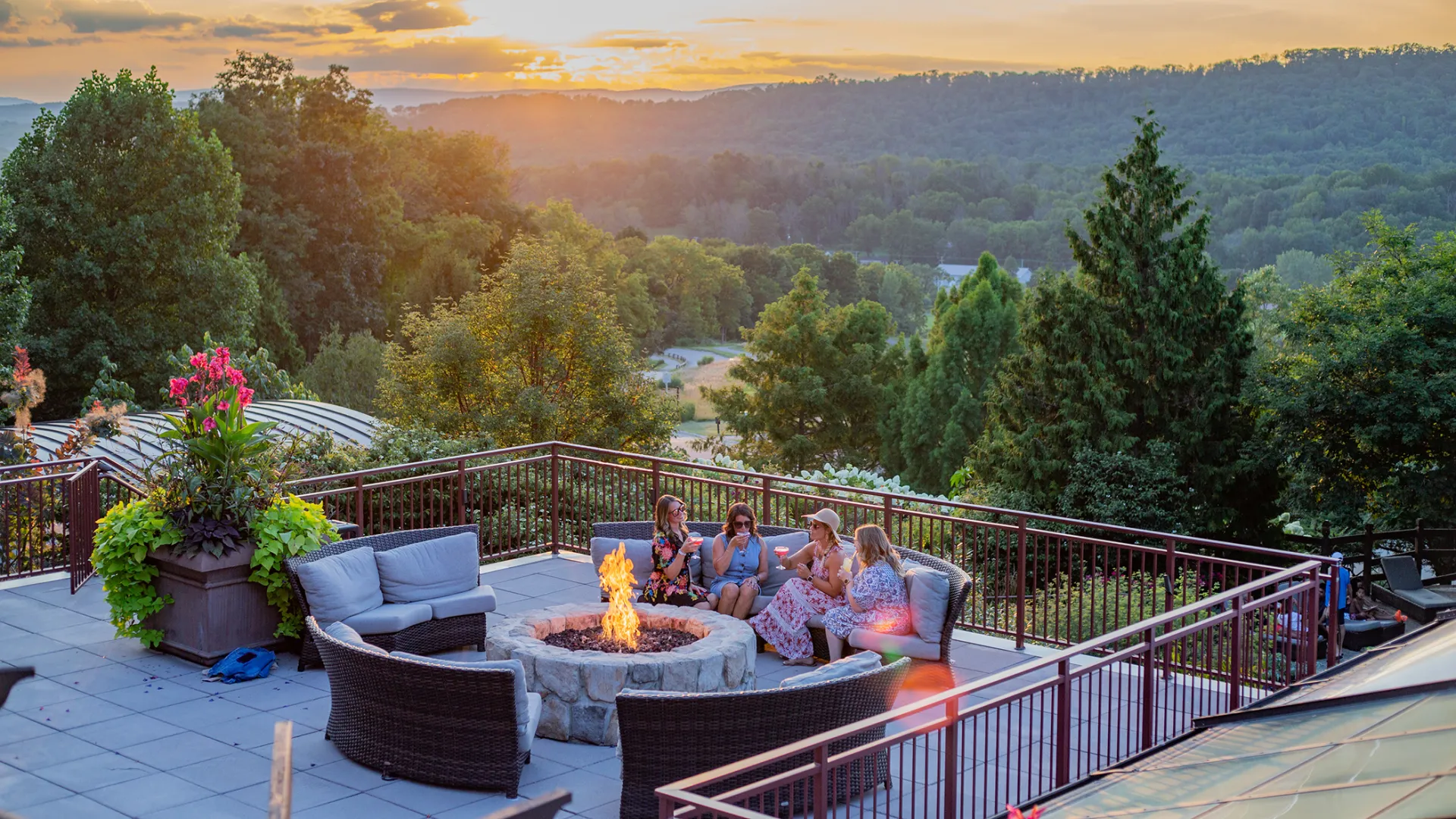 Group of four girlfriends sitting around firepit on Fire &amp; Water terrace overlooking sunset mountain views.