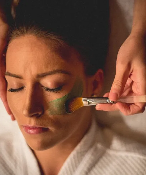 Facialist applying green face mask to woman's face.