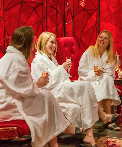 Group of girlfriends in white robes drinking champagne in Reflections Spa's Crystal Room.