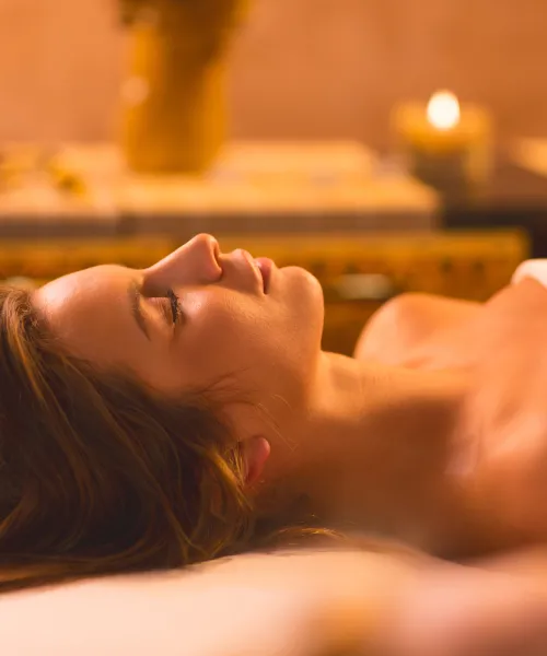 Woman laying in white towel on spa table surrounded by candles.
