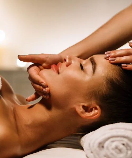 Woman laying on table with facialists hands on her chin and forehead. 
