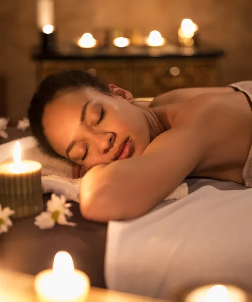 Woman laying on spa table surrounded by little candles.