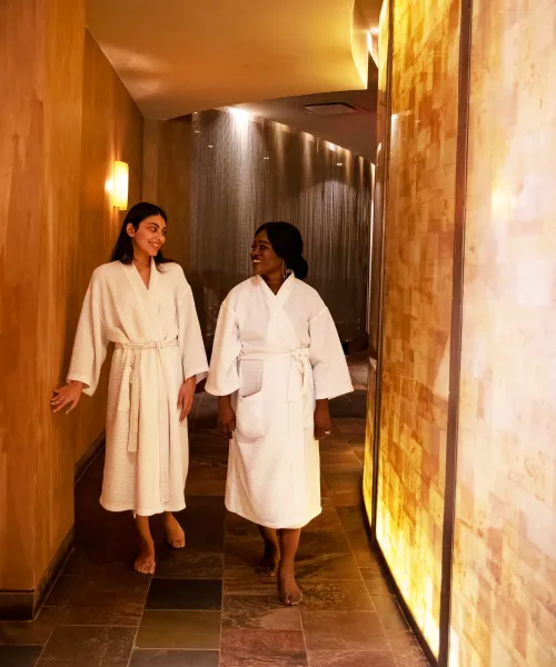 Two women in white bathrobes walking down Elements Spa hallway.