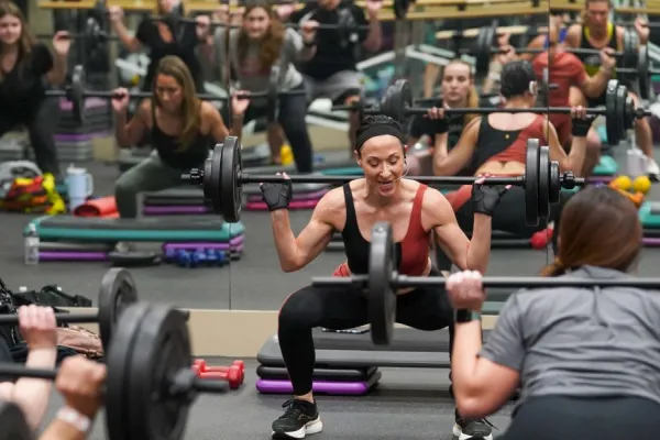 Group of people squatting with barbell over their shoulders.