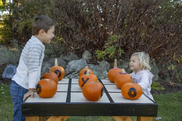 Boy and girl play tic tac toe with pumpkins.