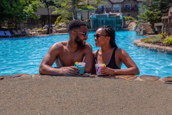 Couple on side of pool drinking rum buckets.