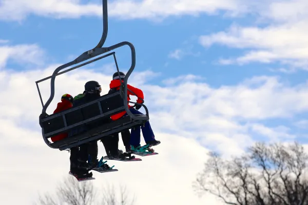 Three people sitting on ski lift.
