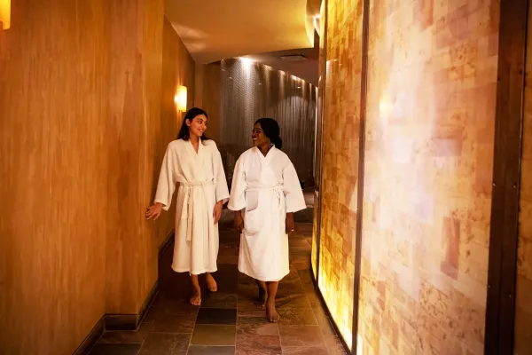 Two women in white bathrobes walking down Elements Spa hallway.