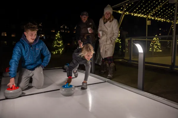 Boy and girl about to push curling stone down ice.
