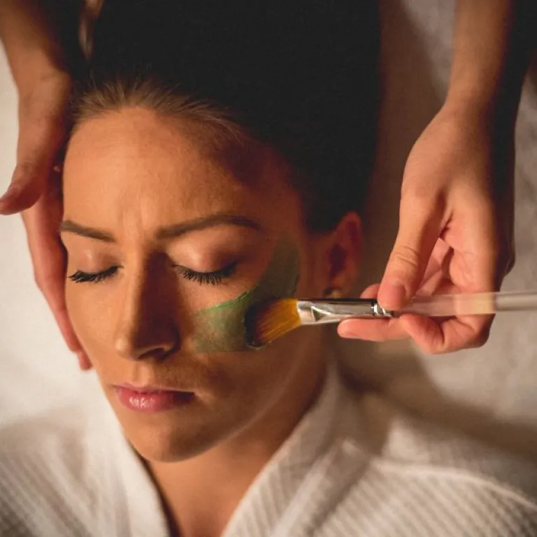 Facialist applying green face mask to woman's face.