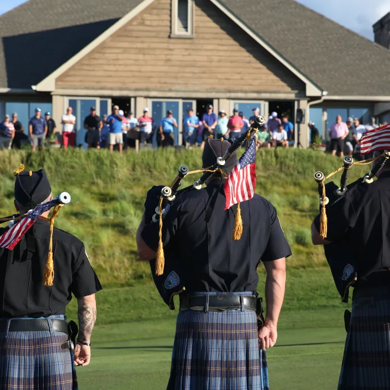 Bagpipers stand with American flags facing towards Ballyowen Clubhouse